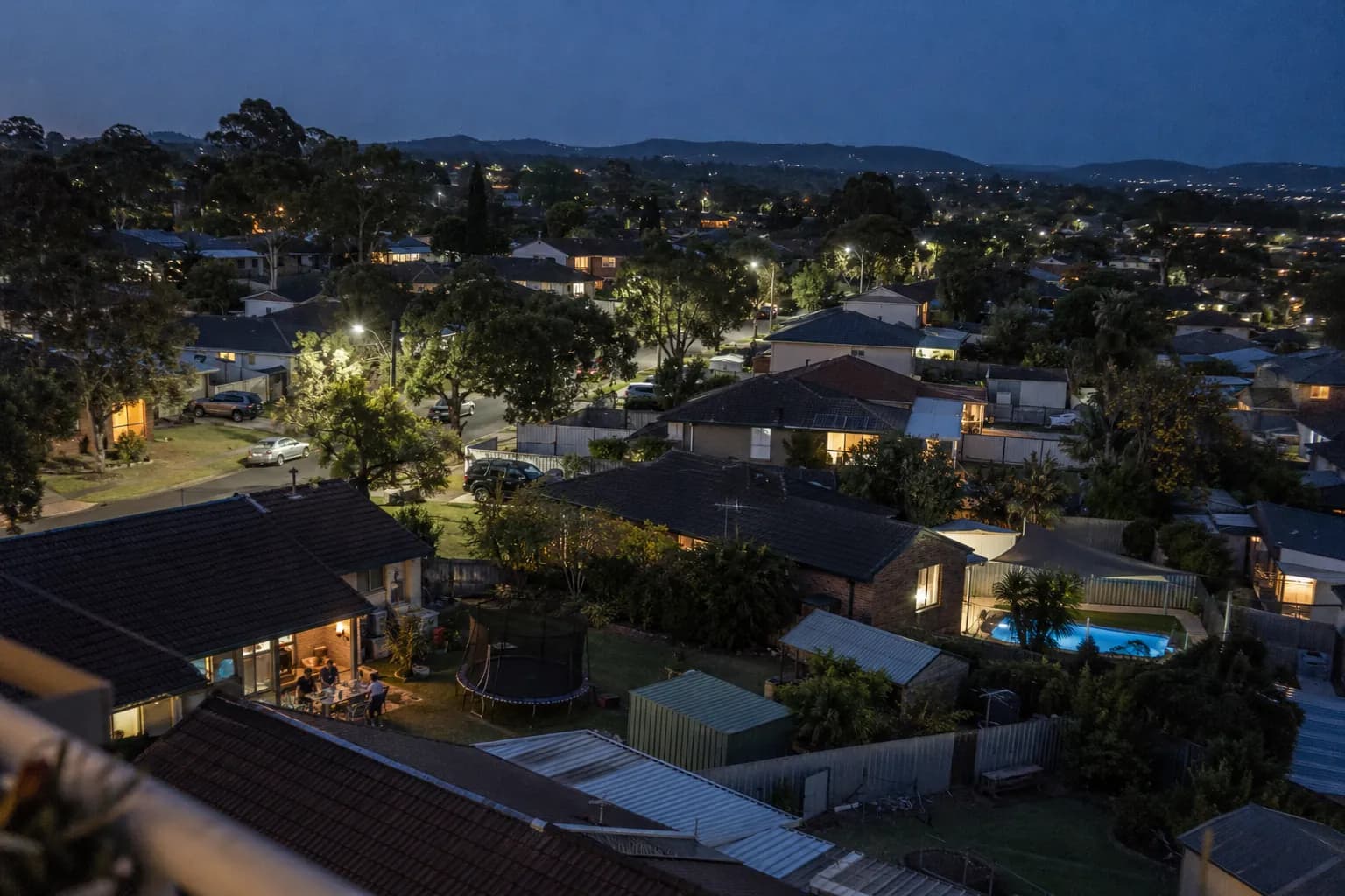 An ordinary suburb from above at dusk, with lights on in the houses and along the streets