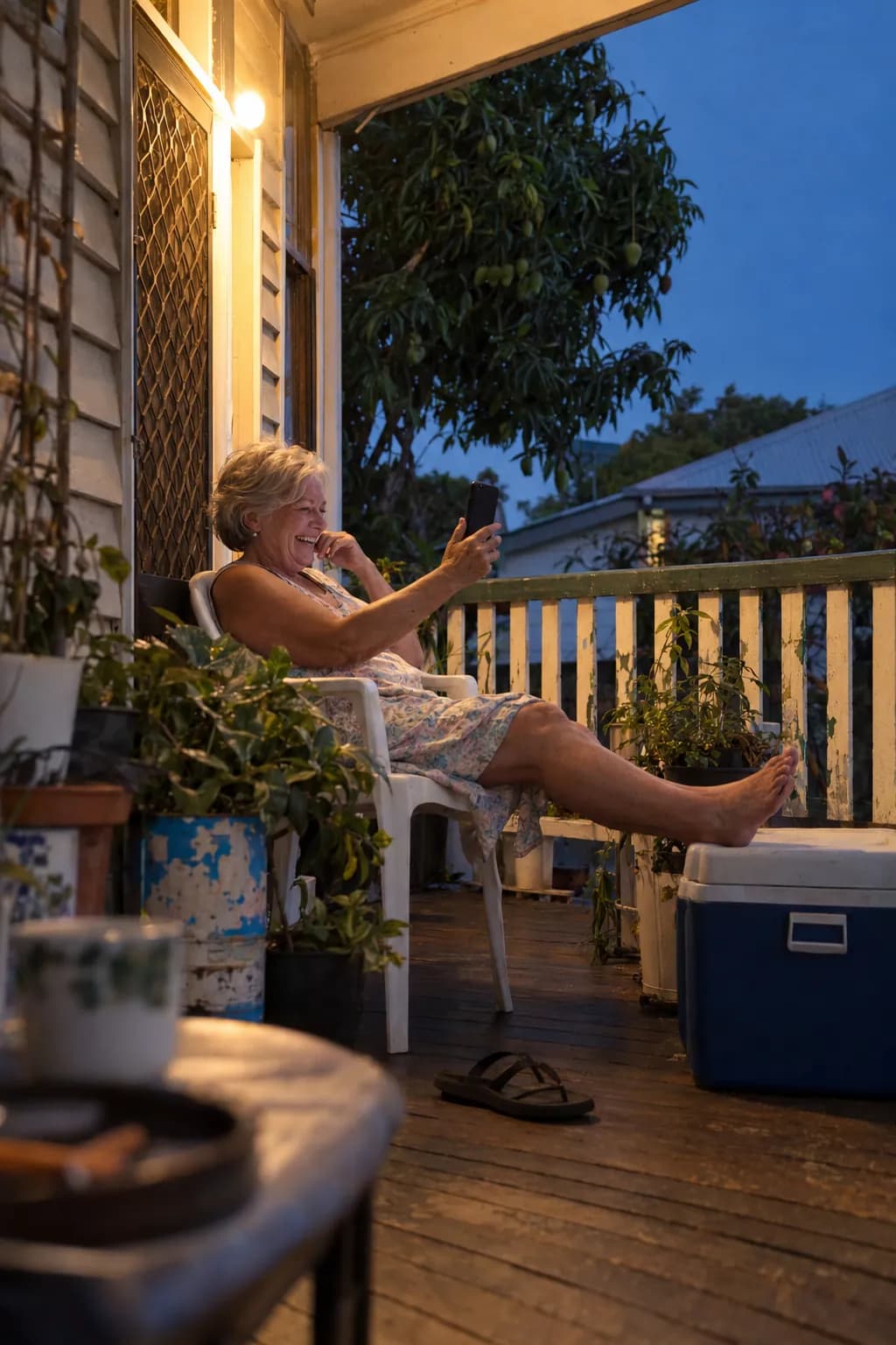 An older woman laughing on a video call on her verandah at dusk